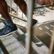 Person går opp en metalltrapp i svarte løpesko med hvit såle og grå sokker. Bildet er tatt gjennom et trappgelender i dagslys.